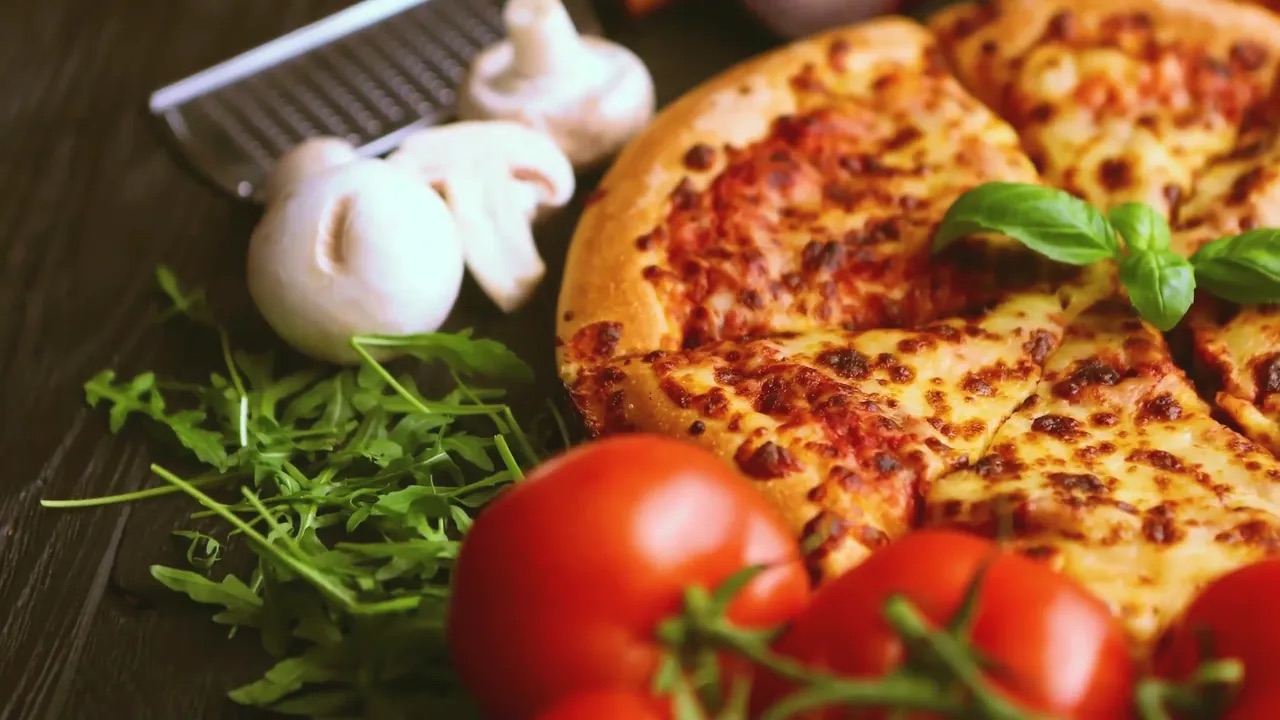 Una pizza d'autore su tavolo di legno con i suoi ingredienti attorno, ripresa che ruota lentamente al procedere dello scroll